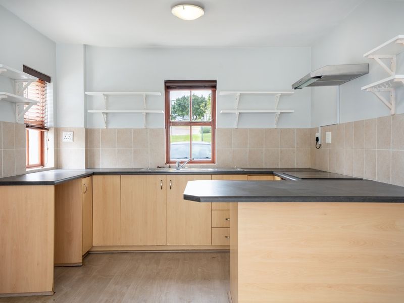 A functional kitchen featuring light wood-finish cabinetry, dark laminate countertops, tiled backsplash, and open shelving, providing a clean and practical workspace.