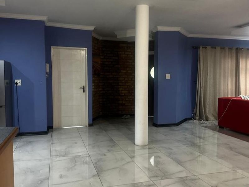 Open plan living area featuring polished marble-look floor tiles, a central structural column, and a decorative exposed brick feature wall.