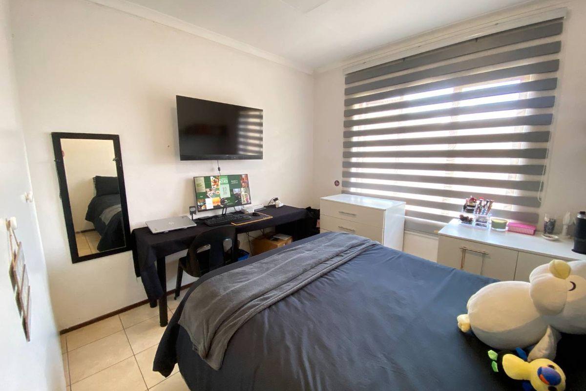 A functional bedroom featuring tiled flooring, a large window with fitted zebra blinds, and wall-mounted television connectivity.