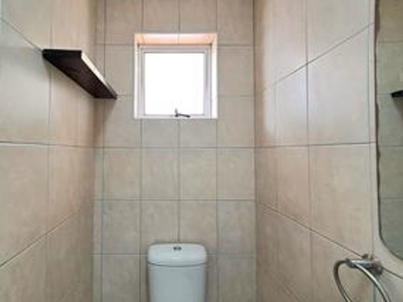 A compact bathroom featuring full-height wall tiling, a modern toilet, and a wall-mounted towel ring.