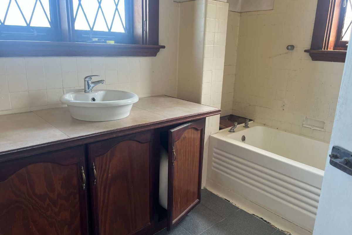A dated bathroom featuring a vanity with a vessel sink, a bathtub, and leadlight windows. The space requires significant renovation and cosmetic updates.