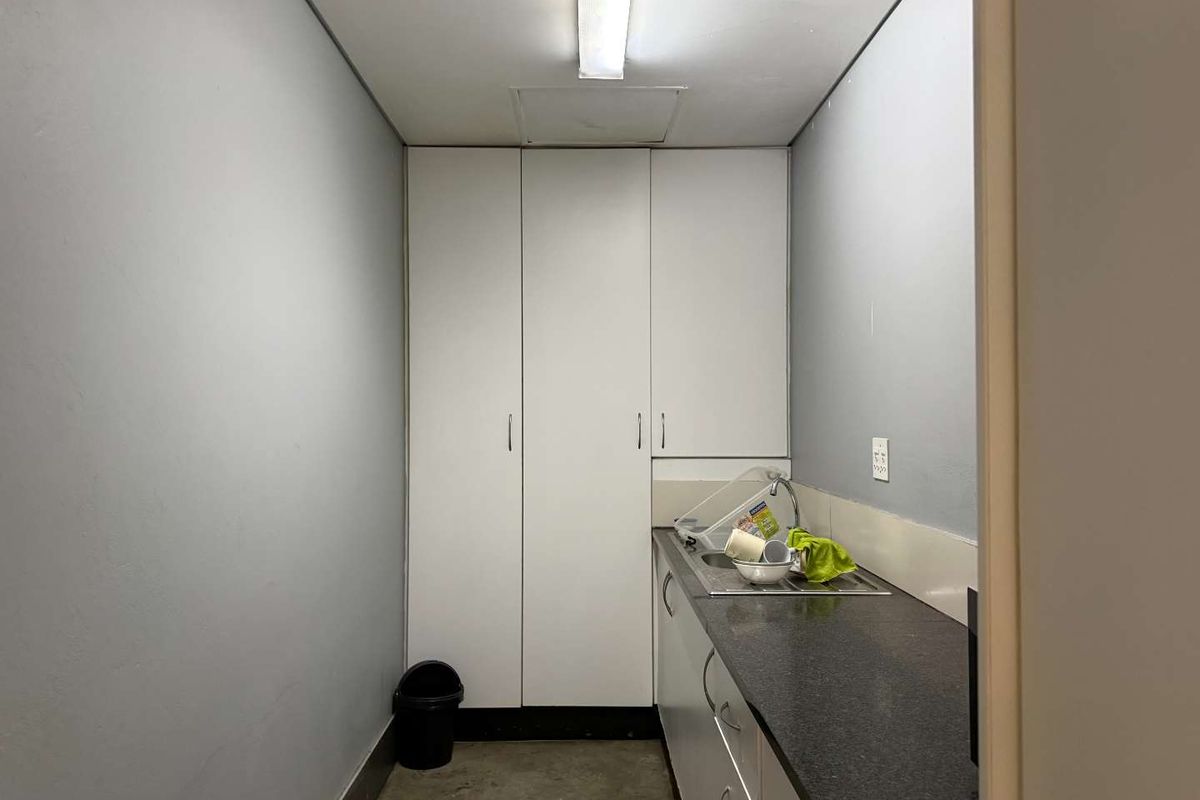 A compact office kitchenette featuring built-in white cabinetry, a dark laminate countertop, and a stainless steel sink.