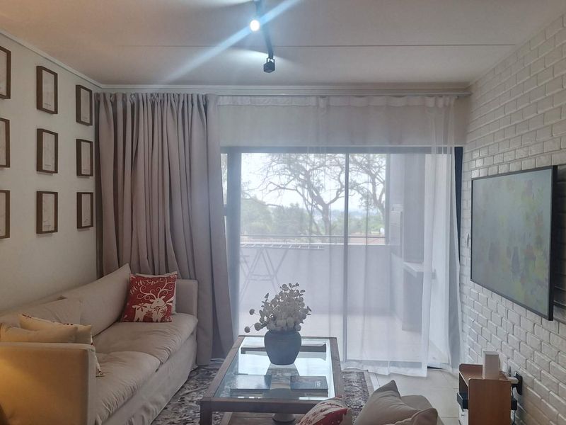 A cozy living room featuring an exposed white brick wall, track lighting, and large sliding glass doors leading to a balcony.