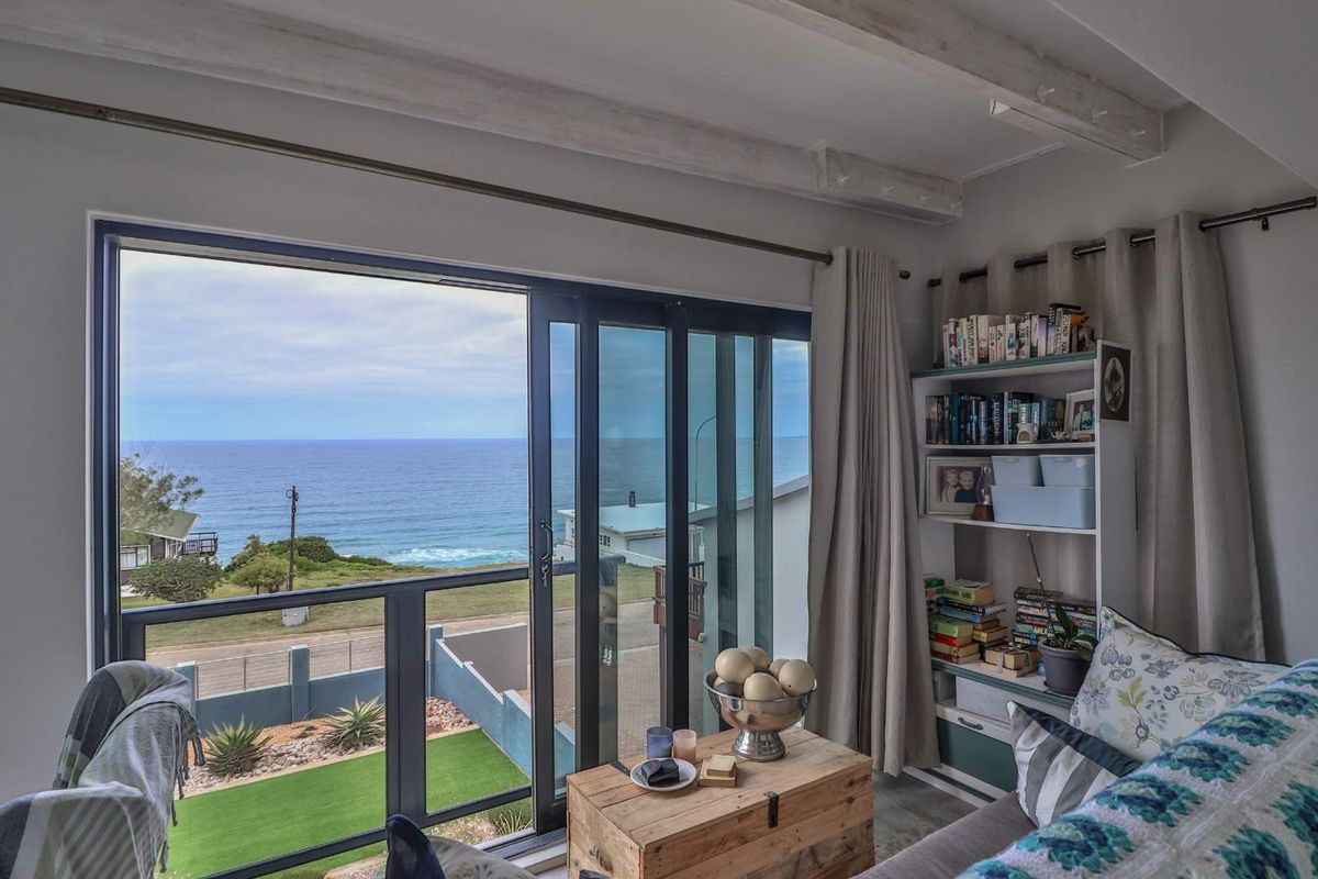 Living room featuring large sliding glass doors that open to a balcony with expansive ocean views and exposed ceiling beams.