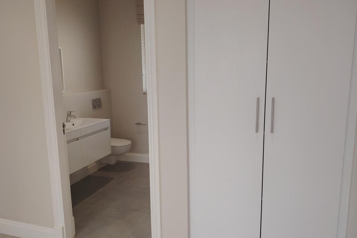 A clean, modern bathroom featuring a wall-mounted vanity and wall-hung toilet, adjacent to a built-in storage cupboard.