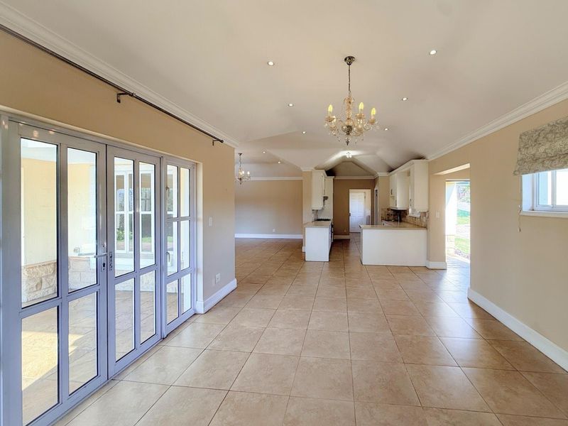 Spacious open-plan living and kitchen area featuring neutral tiled floors, elegant chandeliers, and direct access to the outdoor patio through glass french doors.