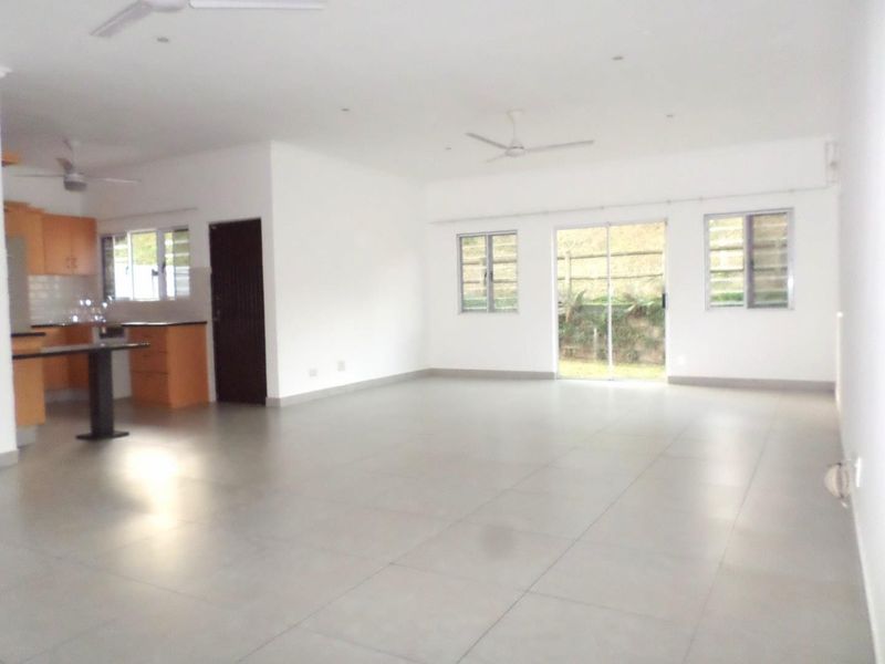 Spacious open-plan living area featuring tiled floors, ceiling fans, and an integrated kitchen with granite countertops and direct access to the rear garden.