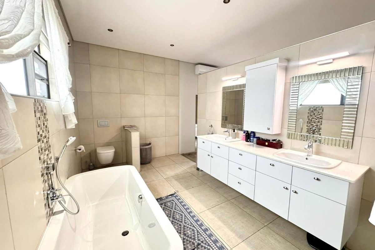 Spacious modern bathroom featuring a freestanding bathtub, double vanity with ample storage, wall-mounted toilet, and neutral floor-to-ceiling tiling.