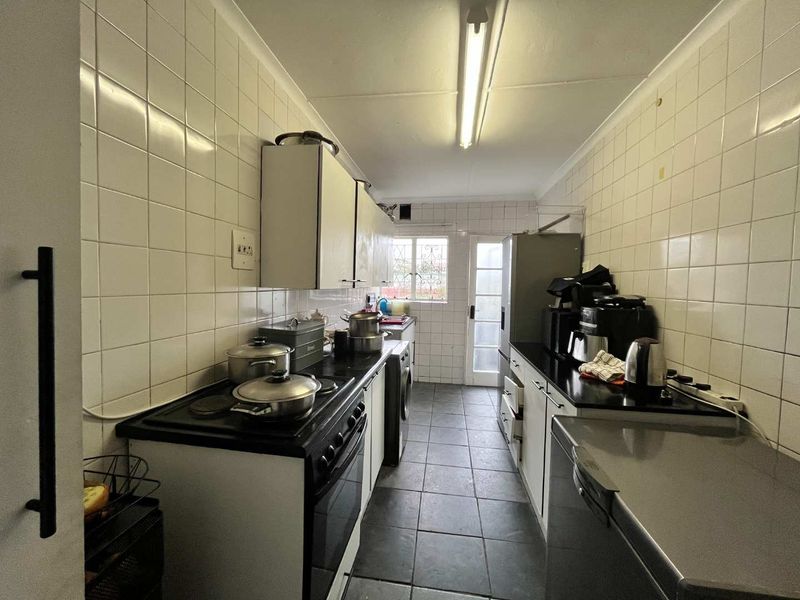 A functional galley-style kitchen featuring tiled walls, dark countertops, built-in cabinetry, and direct access to the rear exterior.