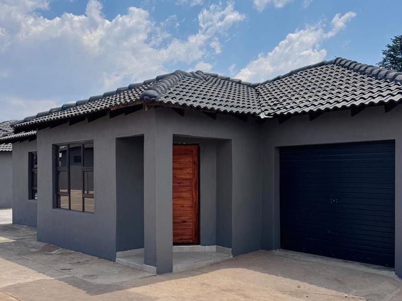 Modern townhouse exterior featuring a dark grey facade, tiled roof, integrated garage, and a natural timber front door.