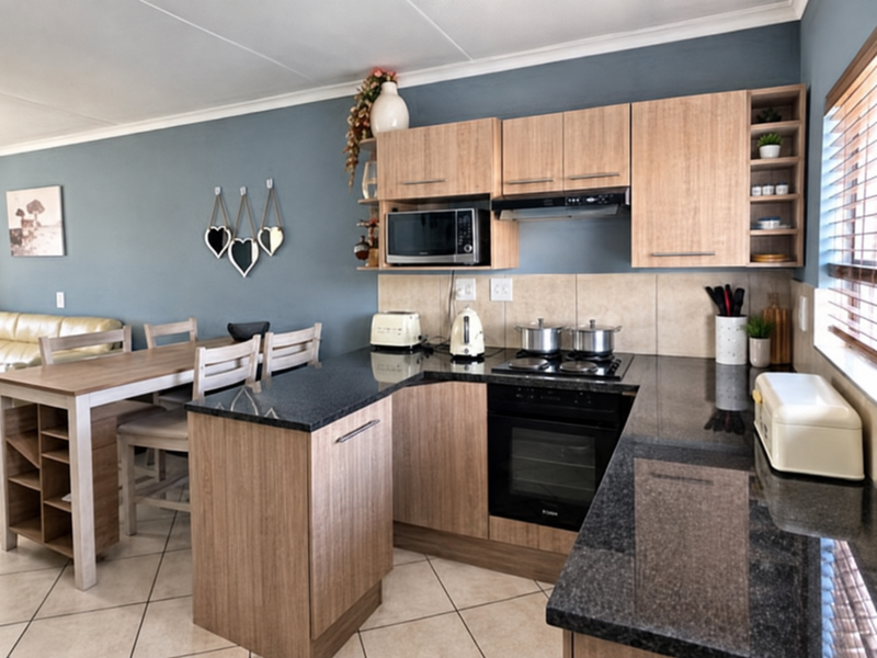 Open-plan kitchen featuring wood-finish cabinetry, granite countertops, built-in oven and hob, and tiled flooring, seamlessly flowing into the dining area.