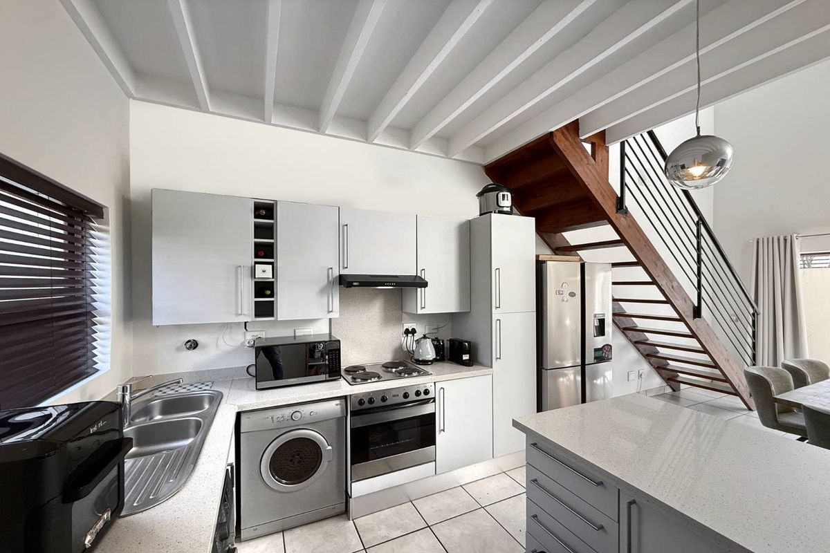 Modern kitchen featuring light grey cabinetry, stone countertops, integrated oven and hob, and a double sink, adjacent to a wooden staircase.