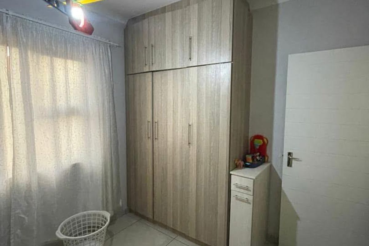 A bedroom featuring built-in wooden cupboards with overhead storage and tiled flooring.