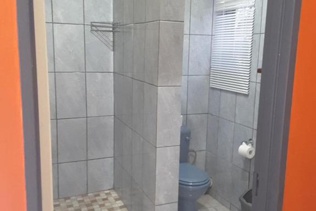 A functional bathroom featuring a tiled walk-in shower enclosure, a toilet, and a window with fitted blinds.