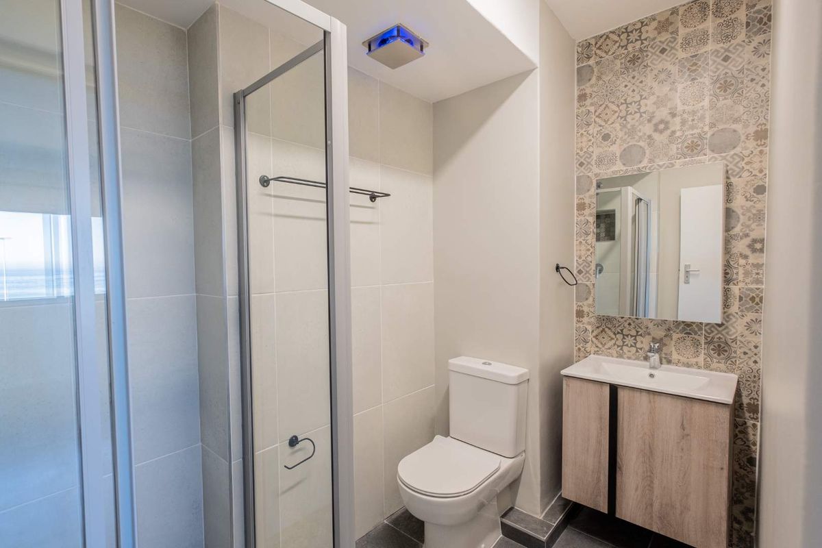 Modern bathroom featuring a glass shower enclosure, a vanity unit with integrated basin, and decorative patterned wall tiling.