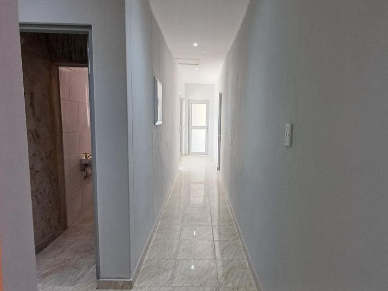 A clean, well-lit hallway featuring neutral wall finishes and light-colored tiled flooring, providing access to adjacent rooms.