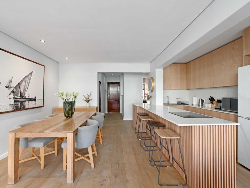 Modern open-plan living and dining area featuring timber flooring, recessed lighting, and a contemporary kitchen with stone countertops and timber cabinetry.