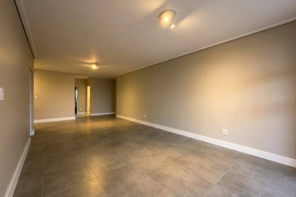 A spacious, empty living area featuring neutral wall tones, modern large-format floor tiles, and clean architectural lines, ready for personalization.