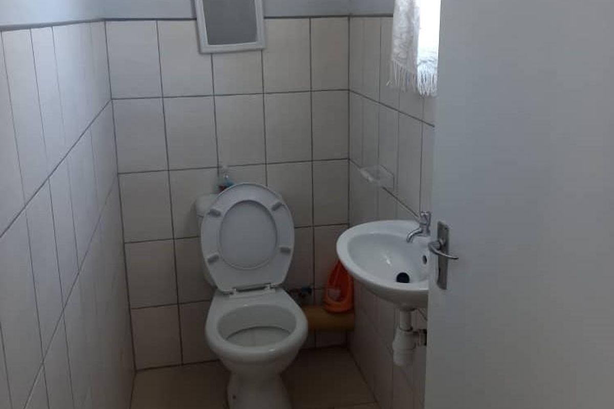 A compact bathroom featuring a standard toilet and a wall-mounted basin with tiled walls and flooring.