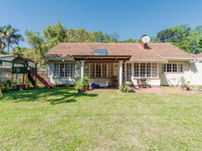Rear view of the house featuring a tiled roof, covered patio area, and a spacious garden with established trees.