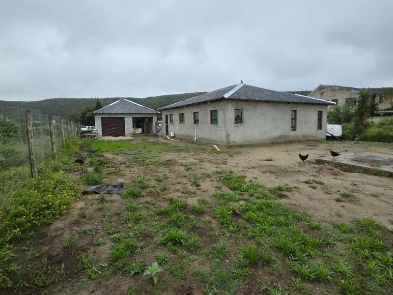 Rear view of the property showing the main dwelling, a detached garage, and an expansive, unlandscaped yard area enclosed by wire fencing.