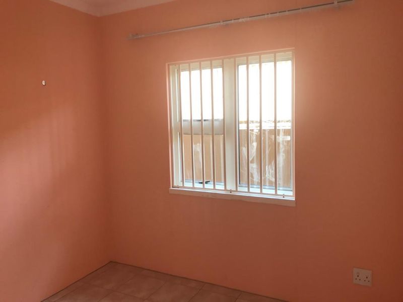 An empty bedroom featuring tiled flooring, peach-colored walls, and a window fitted with security bars.