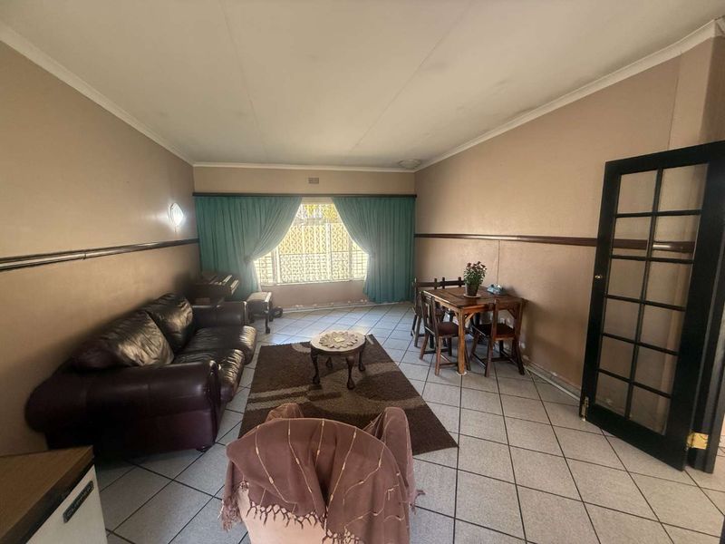 A living room featuring tiled flooring, a chair rail, and a french door, with visible signs of wear on the walls and ceiling.