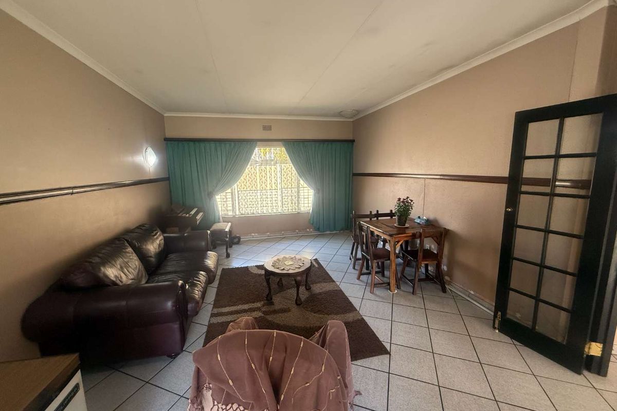 A living room featuring tiled flooring, a chair rail, and a french door, with visible signs of wear on the walls and ceiling.