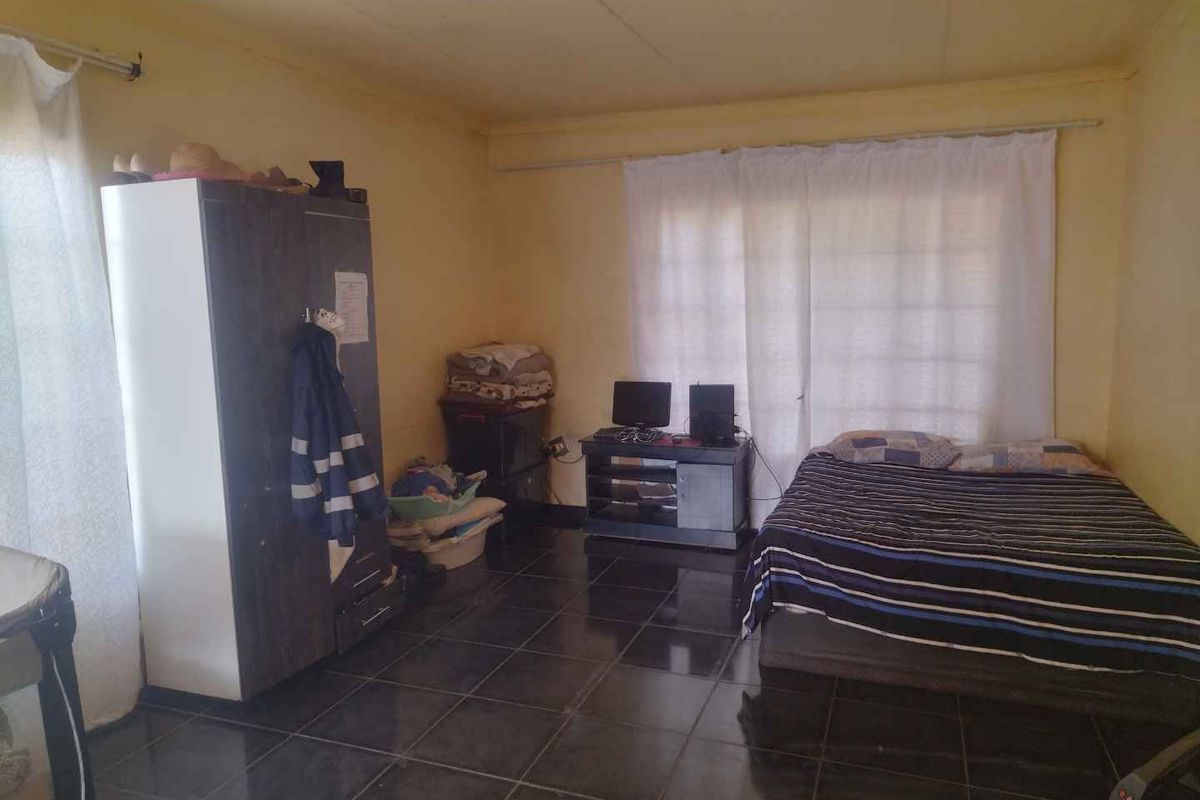 A bedroom featuring dark tiled flooring and curtain rails, currently requiring cosmetic updates to the walls and ceiling to improve its overall condition.