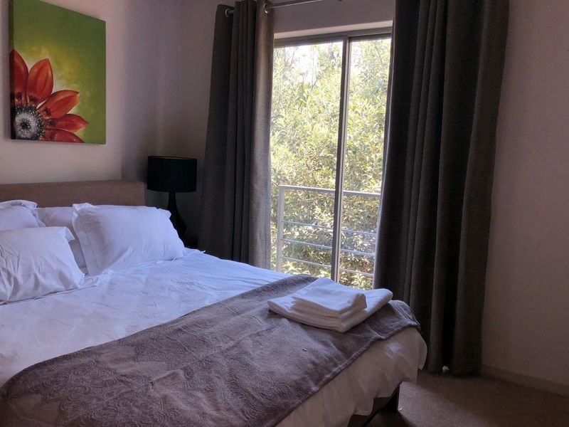 A comfortable bedroom featuring a sliding glass door that opens onto a small balcony with a metal railing, providing natural light and garden views.