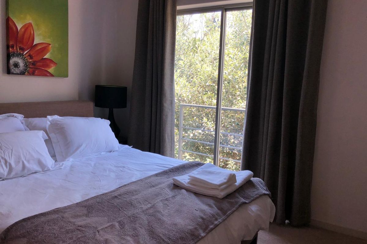 A comfortable bedroom featuring a sliding glass door that opens onto a small balcony with a metal railing, providing natural light and garden views.