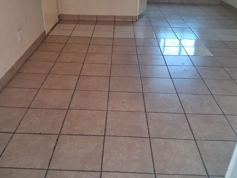 An empty living area featuring neutral ceramic floor tiles, tiled skirting, and an aluminium window frame, providing a blank canvas for interior design.