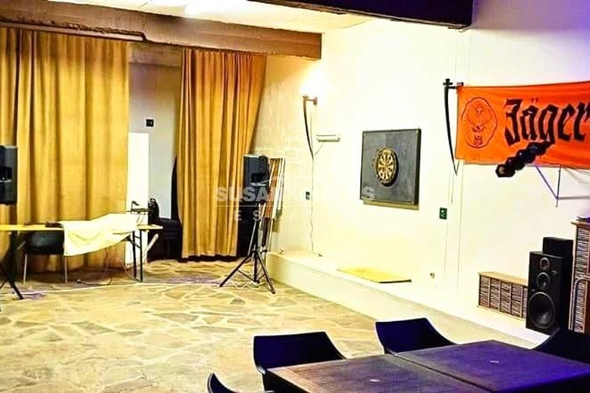 A spacious entertainment area featuring stone flooring, exposed ceiling beams, and built-in wall lighting, suitable for a versatile guest house recreational space.