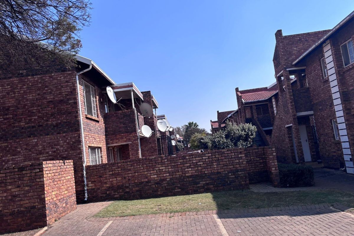 Exterior view of a multi-story apartment complex featuring face brick construction, tiled roofing, and paved communal parking areas.