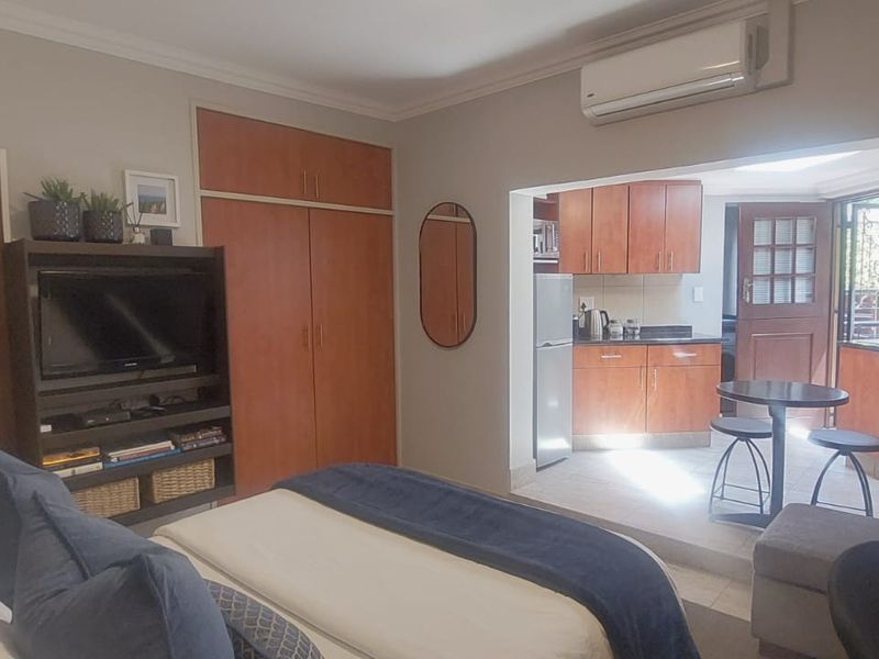 Open-plan bedroom and kitchen area featuring built-in cupboards, air conditioning, and a compact kitchen with granite countertops and tiled flooring.