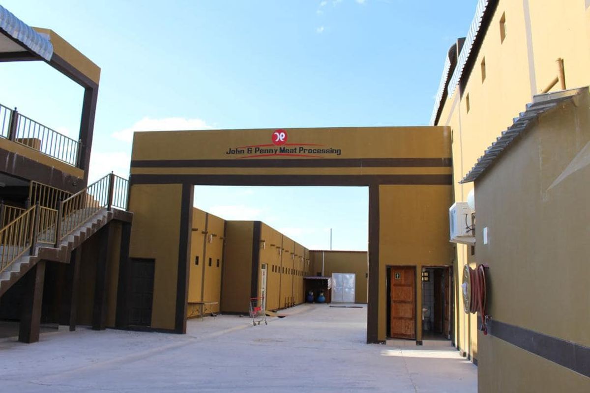Exterior view of a commercial meat processing facility featuring a central courtyard, paved driveway, and multi-level building structure with external staircases.