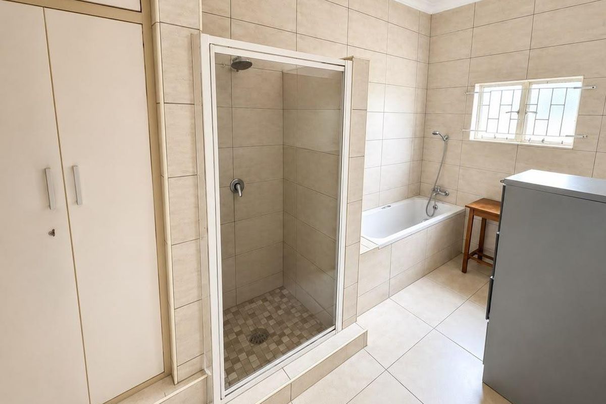 A functional bathroom featuring a built-in shower with glass enclosure, a separate bathtub, and neutral floor-to-ceiling wall tiles.