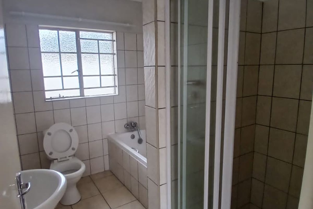 A functional bathroom featuring a separate shower cubicle, a built-in bathtub, a pedestal basin, and a toilet with tiled walls and flooring.