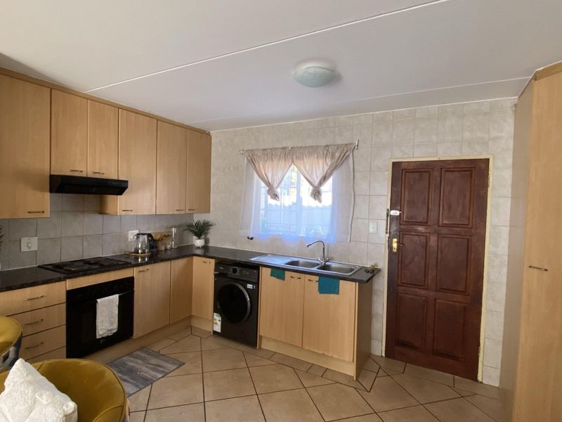 Functional kitchen featuring light wood cabinetry, dark countertops, built-in oven and hob, tiled backsplash, and integrated laundry appliance space.