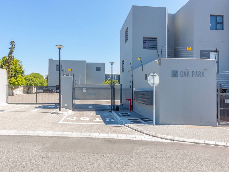 The entrance to Oak Park apartment complex featuring a secure gated access point, paved driveway, and modern exterior facade with integrated security features.