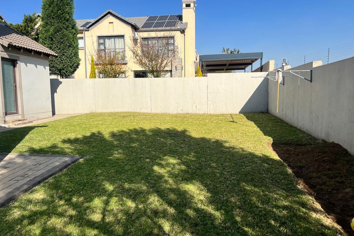 A private rear garden featuring a well-maintained lawn, paved patio area, and high perimeter boundary walls for added privacy.
