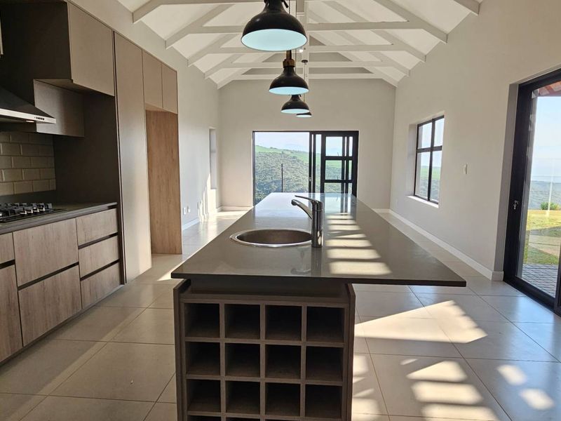 Modern open-plan kitchen featuring a central island with sink, built-in appliances, subway tile backsplash, and vaulted ceilings with exposed rafters, opening to outdoor views.