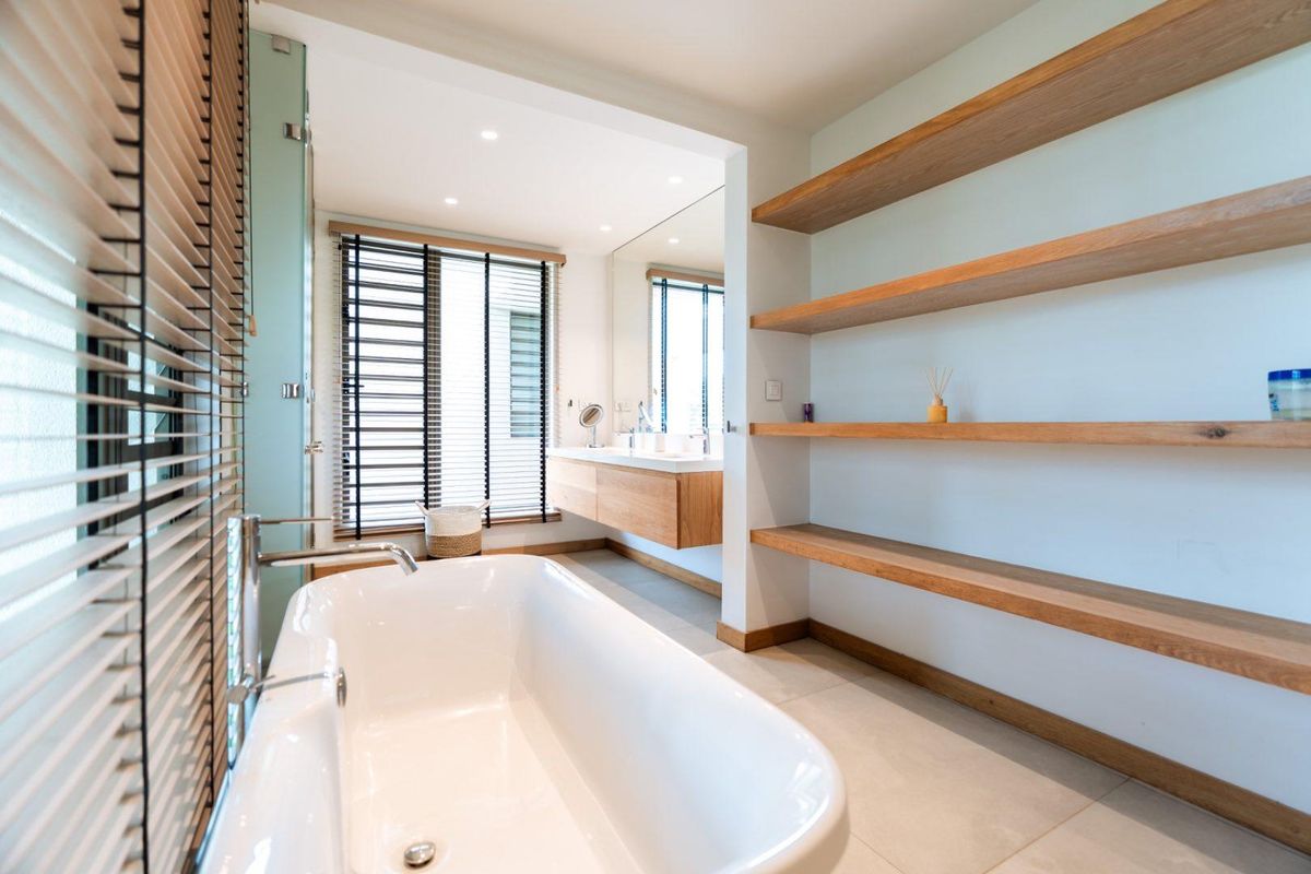 Modern bathroom featuring a freestanding bathtub, floating vanity with dual basins, and built-in timber shelving, finished with contemporary fixtures and neutral tiling.