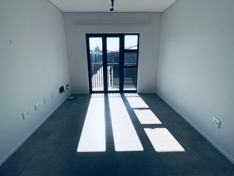 A bright, empty bedroom featuring modern tiled flooring and a black aluminium framed glass door leading to an outdoor area.