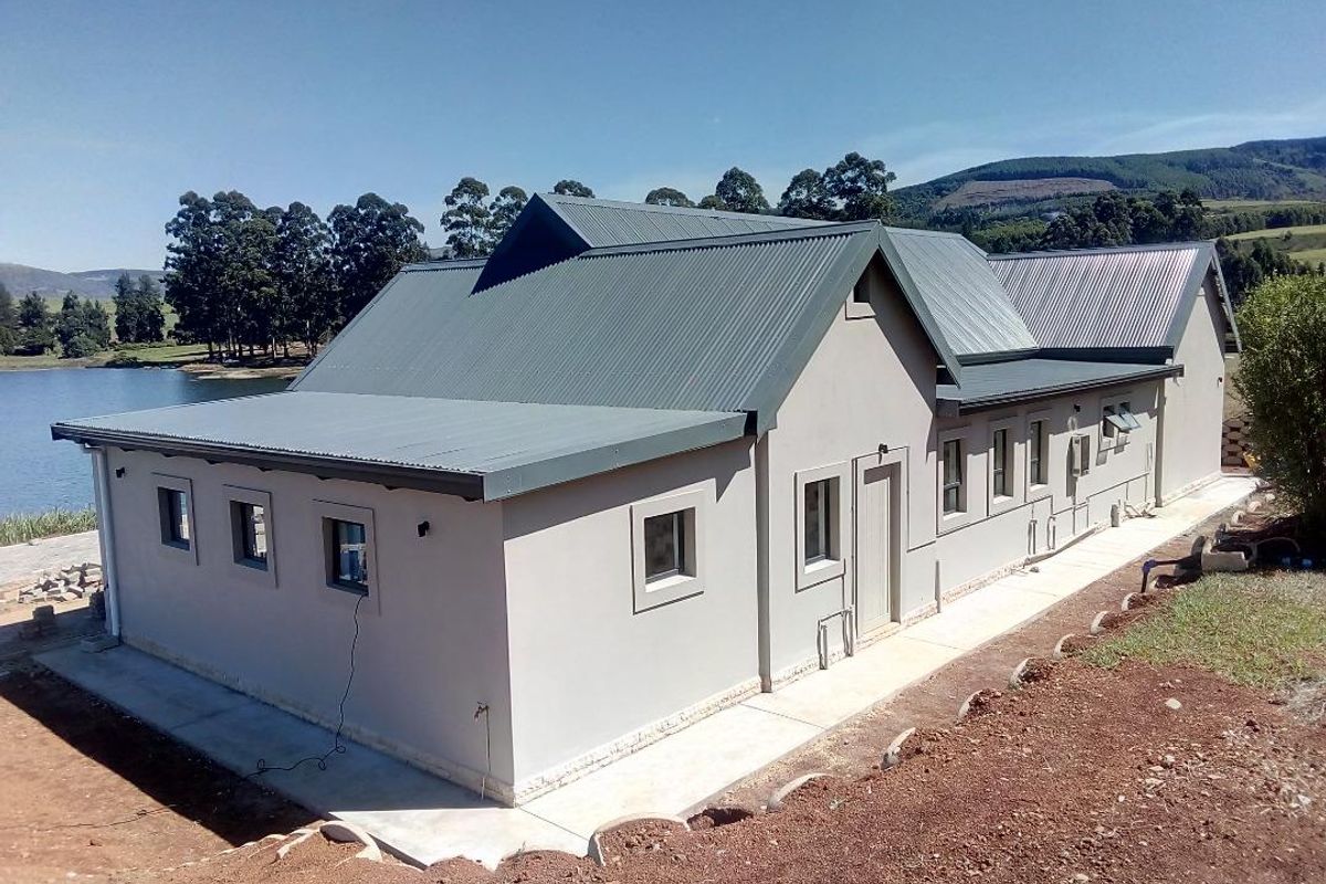 A view of the rear exterior of a modern residential property featuring a metal roof, concrete pathways, and scenic lakeside surroundings.
