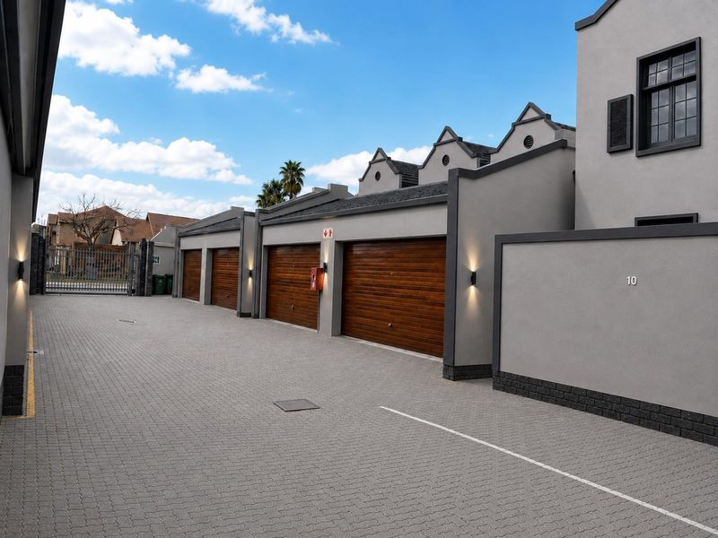 A well-maintained townhouse complex exterior featuring a paved driveway, multiple wooden garage doors, and modern exterior wall lighting.