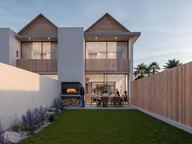 Rear view of a modern townhouse featuring a private garden, built-in braai area, timber fencing, and upper-level balcony with sliding glass doors.