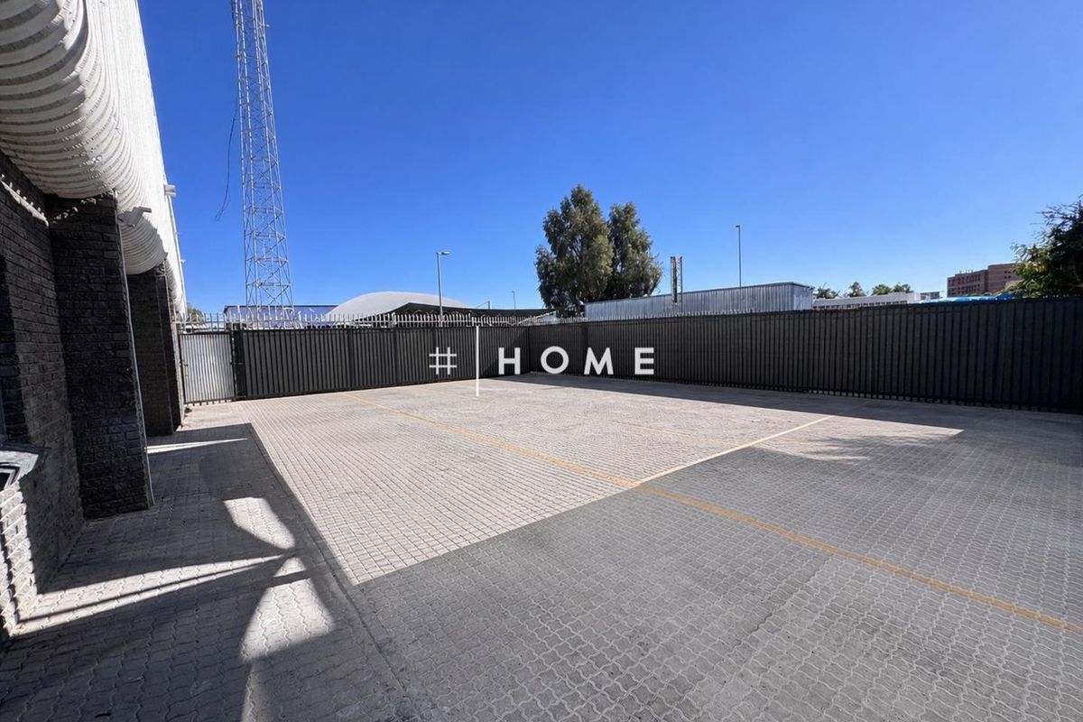 A paved outdoor parking or utility area enclosed by metal perimeter fencing, featuring a clear open space suitable for business operations.