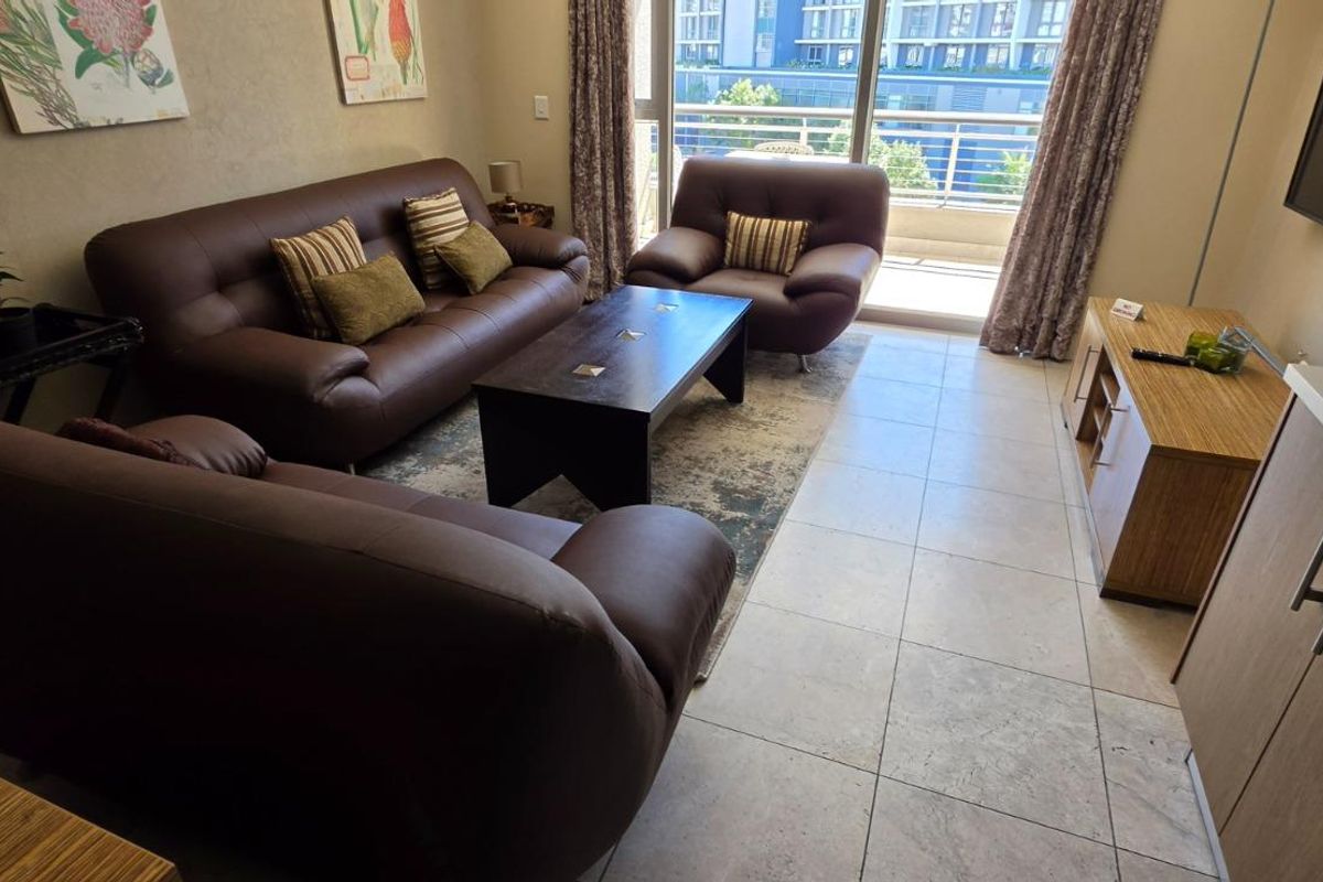 A well-lit living room featuring tiled flooring and direct access to a balcony through large sliding glass doors.