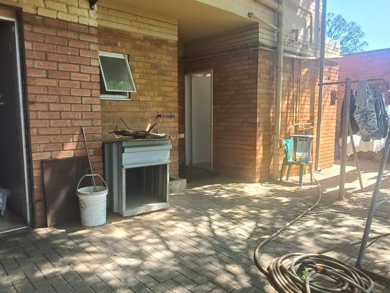 A paved outdoor patio area featuring brick wall construction, a sliding glass door entrance, and an awning window, providing direct access to the rear garden.